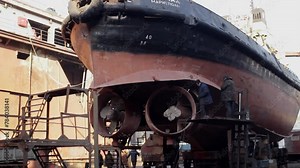 Workers repair ship in floating dock, welding hull, inspecting rudder, applying rust-resistant coatings. Shipyard repairs, maritime maintenance, ship building industry, commercial shipping.