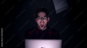 Cybersecurity Hacker violently scatter sheets of paper. Sheets of paper fall on the programmer sitting at the laptop. Portrait of a man behind the monitor in the dark.
