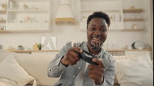 Excited African man playing video games at home, person with joystick smiling. Computer games addiction and overuse, entertainment and leisure in apartment in weekend, young black student has fun