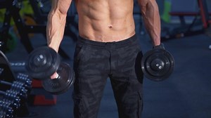 Shirtless muscular man training biceps with dumbbells. Naked torso of a bodybuilder doing functional training with heavy weights. Sport fitness healthy lifestyle concept.