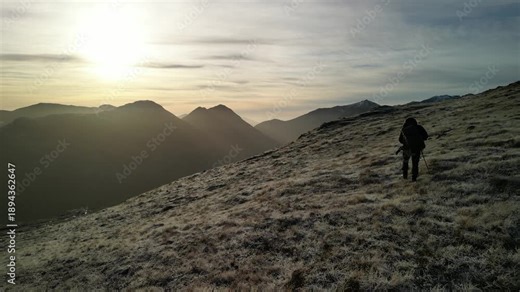 Glen Coe, Scottish Highlands - aerial over the mountains in winter with hill walker hiking away towards the setting sun