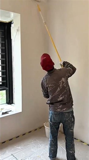 painting the interior walls of a house using a long roller brush to apply white paint evenly now