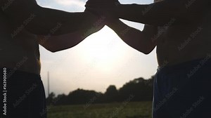 Friendly handshake of two unrecognizable muscular white men with sun shine at background. Shaking of male arms outdoor. Two strong guy meeting outside. Teamwork and friendship. Close up Slow motion