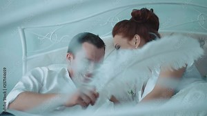 Young beautiful couple having fun in bed, she pinching him on the cheek, laughing, passing the camera along the bed, close-up, slow motion