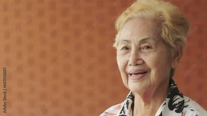 Close-up face of a asian modern grandmother, in a half-body portrait pose against a rustic brick wall background, shows positive aged life, healthy wellbeing for retired senior with happiness.