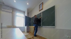 Teacher writes formulas on chalkboard near window. Timelapse