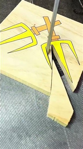 Carving knife traces yellow trident design on wood