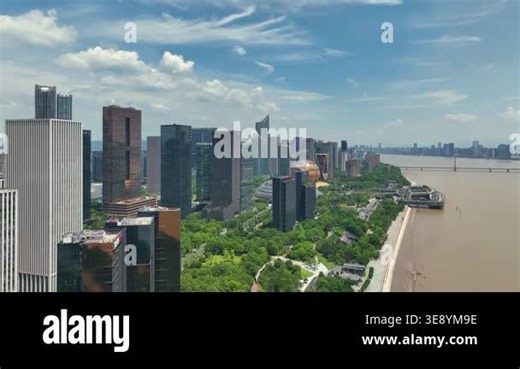 A scenic high angle view of a modern city skyline sitting beside a wide flowing river under blue sky
