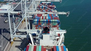 Drone flies over container ship being unloaded at terminal