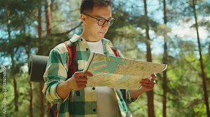 Asian man tourist walking in forest camp. Young hiker traveling and hiking alone, guy using map and wearing backpack. Summer tourism, wild nature.