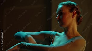 Cinematic close up shot of beautiful ballerina in ballet tutu performing on dim opera stage. Female ballet dancer on choreography rehearsal in theater, practices elegant movements. Classical ballet.