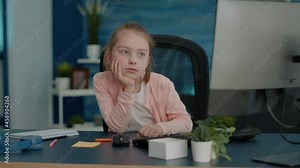 Tired child attending online class lesson on computer at home. Young girl falling asleep while looking at monitor for remote school courses. Exhausted pupil learning on internet