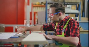 Carpenter working with meter or rule taking measures on wood using pencil.