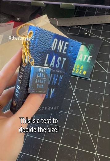 One of the new products i’ve been testing out for a bit! I think i’ve nailed down the size… What do you think? Yes? 🤔 These would be officially licensed as well with all my authors and current designs 🫶 I’ll be getting a WAY better printer and sealing them with a waterproof glossy coat 😊#keychains #bookish #onelastrainyday #bookloversoftiktok #bookwallet