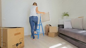 Young woman taking stepladder and hanging it on the wall