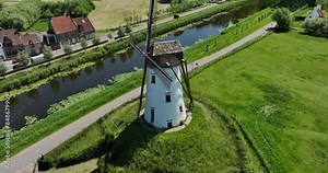 Damme, Belgium, June 2022. Drone orbits the Schellemolen windmill surrounded by lush green fields and Damse Vaart canal.