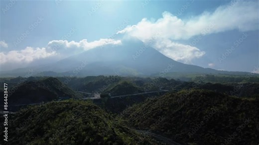 4k aerial footage of Mount Merapi from a distance of 2.5 miles on a hot and cloudy day. Aerial panorama of Mount Merapi during the day with white clouds and a winding road in the foreground Stock Video