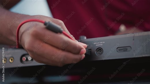 black DJ adjusting jack during soundcheck, tight closeups of fingers inserting red cable into DIN socket, quick patch swaps and channel checks, ambient crowd murmur and street set tension before drop