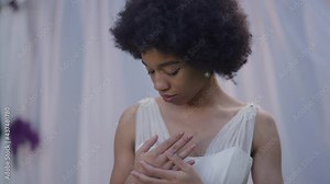 Young charming slim African American bride caressing ring on finger smiling and dreaming. Portrait of happy confident woman in white wedding dress standing at altar. Newlywed rejoicing marriage