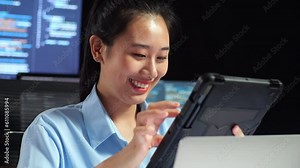 Close Up Of Asian Female Programmer Using Tablet While Writing Code By A Laptop Using Multiple Monitors Showing Database On Terminal Window Desktops In The Office