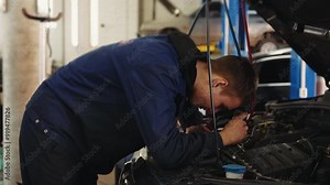 Young auto mechanic under the hood of a car with a flashlight checks the condition of the engine