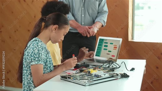 Teacher standing while explain coding and robotic construction. Diverse teenager fixing mother board and using electronic tool while looking at laptop display programming code screen. Edification