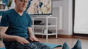 Close up of aged man doing stretch exercise on yoga mat. Retired person stretching arms and legs muscles to start workout activity. Senior adult doing gymnastics and aerobics training.