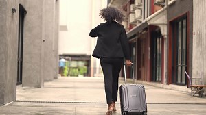 Download A black woman is getting ready for work in an office uniform in a public downtown area, carrying all her work equipment including a computer and a phone. for free