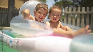 Two little brothers playing together in the pool on a sunny day of summer, in a sweet and happy way