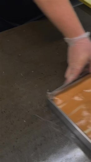 3.6K views · 966 reactions | Ever wonder how those luscious ribbons of caramel find their way into our vanilla caramel fudge? Here’s Chris at work—masterfully layering sheets of golden caramel into a fresh pan of creamy vanilla fudge. It’s a small behind-the-scenes glimpse, but it’s how every slice gets that perfect strip of sweet and buttery goodness. #DouglassCandies #CaramelFudge #WeMakeTheCandyWeSell #Since1919 #CandyMaking | Douglass Candies | Facebook