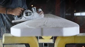 Surfboard making, Shaper using a foam sander tool on the bottom of the surfboard. Concept of craftsmanship, small business in America, craftsman at work.