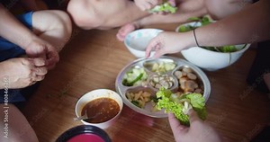 A group of people are sitting on the floor and eating food. There are several bowls of food on the table, including a bowl of salad. Scene is casual and relaxed
