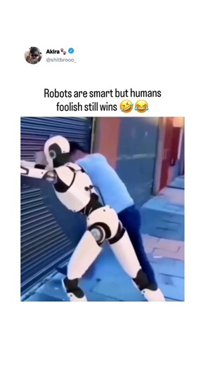 𝗔𝗸𝗶𝗿𝗮🐾 on Instagram: "This 14-second clip captures a surprisingly funny moment between a human and a humanoid robot in an urban alleyway. A man wearing a blue shirt repeatedly nudges a white humanoid robot against a closed metal shutter. Each time, the robot tries to respond logically—awkwardly pushing back, recalculating its balance, and attempting to stay upright—before eventually stumbling away in confusion. The moment is captioned to highlight how human unpredictability can still outsm