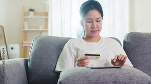 Asian woman using tablet, credit card buy and purchase e-commerce internet in living room from home when social distancing stay at home and self quarantine time, online shopping, coronavirus concept.