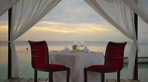 Romantic evening table for two persons on the beach at sunset on the background of beautiful clouds