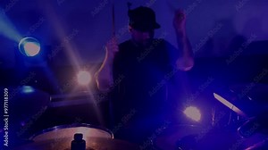 The drummer cool plays the rock concert. A man energetically drumming on stage with vibrant lights illuminating behind him. A drummer performing live, surrounded by colorful stage lights.