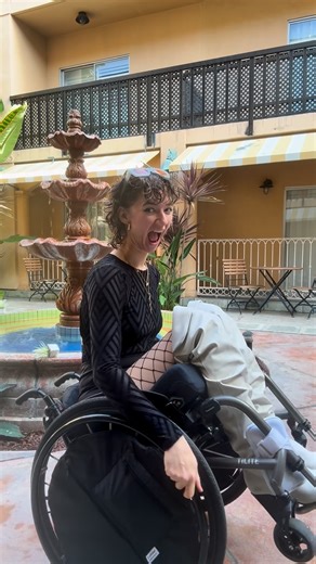 Aly Corvin on Instagram: "Trusty dusty @forever21 bodysuit coming thru… Alt text: A woman in a wheelchair shows off her wheelie in front of a fountain in a courtyard. Captions are on screen for accessibility. #Wheelie #Silly #ChristmasWish"
