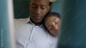 Attractive couple on train journey. Man uses mobile phone while woman sleeps against his shoulder.