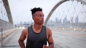 African American man working out by jogging across the 6th Street Bridge in Los Angeles at dawn on an overcast morning. Downtown LA can be seen in the background. Jogger has a deformed left hand.