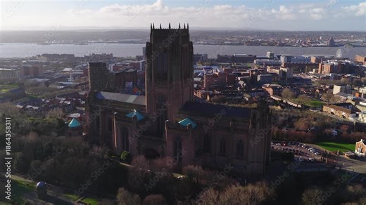 Aerial sunrise scene in Liverpool, UK. The drone glides past Liverpool Cathedral, turrets, and tower, with the River Mersey, Echo Wheel, Tate Liverpool, and Museum of Liverpool visible.
