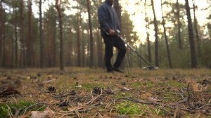 treasure hunter searching for old objects using metal detector in forest