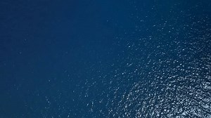 Over The Ocean. Aerial top down view of sea surface with deep blue water, moving forward. Navy blue azure turquoise sea water texture from high altitude as background