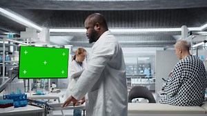 Green screen next to black medic studying data for drug testing in lab, evaluating dosage and potential side effects. Checking chemical reactions and safety to support science breakthrough. Camera A.