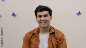 An excited young guy saying "Wow" and giving a wide toothy smile at the camera. Handsome Indian teenager showing "wow" gesture while sitting against a decorated wall - expressions/emotions concept