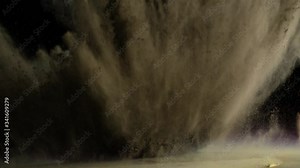 In real slow motion footage against a black background, grey powder bursts into frame from below like a firework. Side Shot.