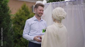 Portrait of happy groom putting wedding ring on finger of bride smiling. Loving Caucasian man getting married with Middle Eastern woman on spring day outdoors in garden. Happiness and love