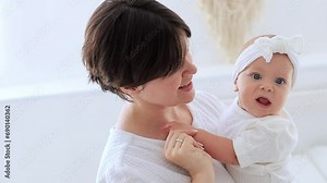 mom gently hugs her baby daughter kissing and admiring them, happy family, mom with baby on the bed, maternal love and care, mom on maternity leave playing with the baby