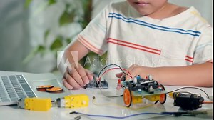 Asian kid boy plugging energy and signal cable to sensor chip with Arduino robot car, Little child remotely learn online with car toy, STEAM education AI technology course school learning lesson