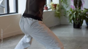 African American black male wearing karate pants, shirtless, in an empty studio with windows, moves through a sword kia as camera floats from floor to hands. Slow motion HD, medium frame.