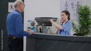 Medical assistant using landline phone call at hospital reception desk, talking to patients on cord telephone to make healthcare appointments on computer. Working at health center.